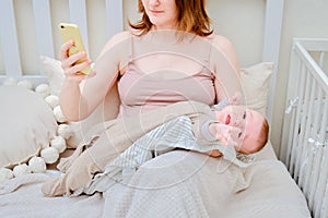 A woman mother breastfeeding a crying infant baby with a phone in her hand. Mom problems with breastfeeding and finding a solution