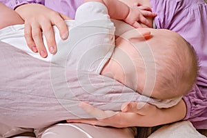 Woman mother breastfeeds an infant baby sitting on a home sofa. Mom feeds milk toddler baby in living room