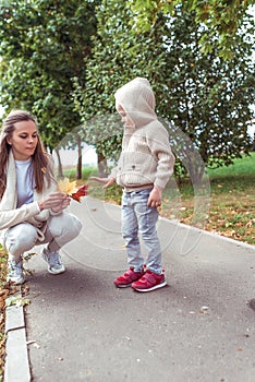 Woman mother collects wedge leaves for child, little son boy of 4-5 years old, autumn trees background, on a weekend