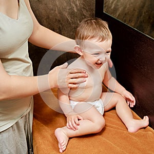 Woman mother giving massage to happy toddler baby sitting on brown