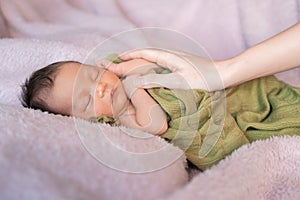 Woman mother hand touching baby infant sleeping on soft furry bed in studio.