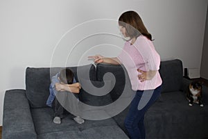 Woman, mother, scolding her son, showing with an accusatory hand, kid sitting with her hands closed on the couch, concept of