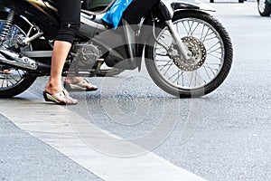 Woman on motorbike with sandals on feet stands on busy street of Ho Chi Minh City, Vietnam
