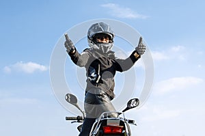 Woman on motorcycle against blue skywith thumbs up because something good has happened