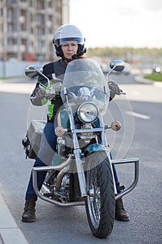 Woman a motorcycle driver sitting on classic chopper bike, holding steering wheel, open face helmet, full length