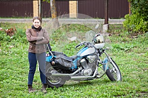 Woman motorcycle driver standing close to her bike, leather jacket, crossed arms