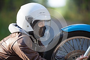 Woman in a motorcycle helmet clutching motorbike spoked wheel looks at a headlight