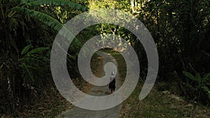 Woman in motorcycle helmet walks along the road in the middle of the green dark jungle