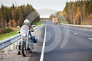 Woman on a motorcycle resting on the roadside of a country highway with empty road