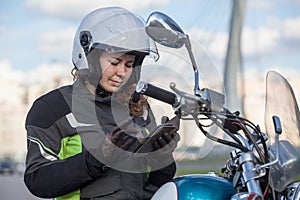 Woman motorcycle traveler finding the location in navigator device, sitting on her bike