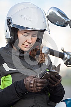 Woman motorcyclist traveller finding the location in navigator device, sitting on her motorbike
