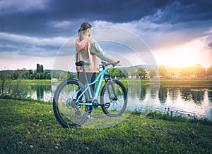 Woman with mountain bike near lake and overcast sky in spring