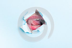 Woman mouth wearing gloss thru ripped paper hole