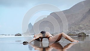 Woman moves plastically dancing on the sand near the ocean against the mountains and black sand