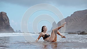 Woman moves plastically dancing on the sand near the ocean against the mountains and black sand