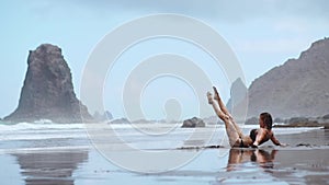 Woman moves plastically dancing on the sand near the ocean against the mountains and black sand