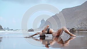 Woman moves plastically dancing on the sand near the ocean against the mountains and black sand