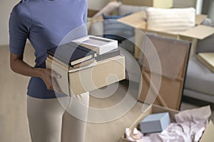 Woman moving into new apartment holding and unpacking her belongings with cardboard boxes