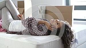 Woman Moving Into New Home Using Mobile Phone Lying On Bed