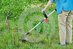 Woman mowing grass with cordless trimmer in garden