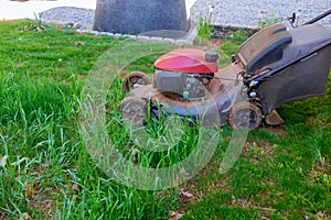 It woman mowing green lawn in a backyard with a lawnmower near the house on a sunny day