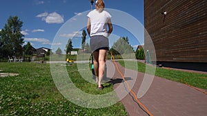 Woman mowing lawn in backyard of his house. Gimbal movement back follow