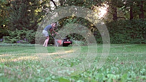 Woman mowing lawn in residential back garden on sunny evening. 4K