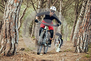 Woman with mtb enduro bike going down mtb trail with her australian shepherd dog