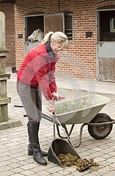 Woman mucking out in a stable yard photo