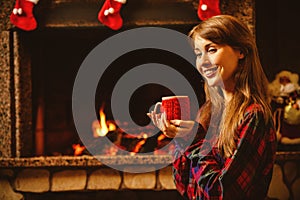 Woman with a mug by the fireplace. Young attractive woman sittin