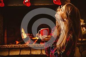 Woman with a mug by the fireplace. Young attractive woman sittin