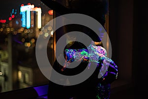 Woman in multi-colored drops of ultra-violet paint with Neon String Lights. Fluorescent body art. UV colors on the girl