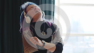 A woman with multi-colored hair in headphones listens to music and dances on the floor in the living room. Energetic