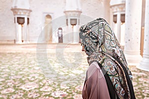 Woman in Muslim prayer room in mosque. Young lady wearing headscarf. Traditional carpet and Arab architecture.