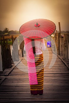 Woman Myanmar holding traditional red umbrella on U Bein wooden