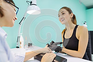 Woman in nail salon receiving manicure by manicurist, closeup manicure process. Nail and hand care in beauty salon.