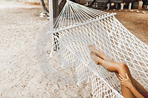 Woman naked legs in white hammock on tropical beach. Travel, leisure, vacations