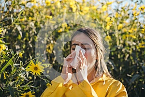 Woman with napkin fighting blossom allergie outdoor. Portrait of an allergic girl surrounded by seasonal flowers in