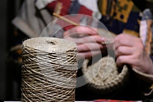 Woman in national rural clothes knits household items from a rope with big reel rope close-up