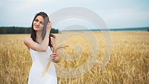 The woman in a national white shirt holds in hand the ripened wheat ears on a gold field background. harvest