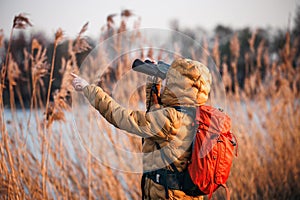 Woman naturalist with binoculars is looking for animals and birds at lake