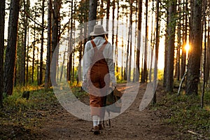 Woman naturalist in orange overalls with backpack on ecological hiking trail in forest