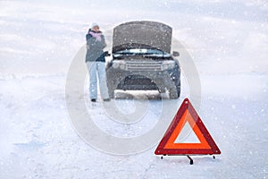 Woman near a broken machine freezes. Around a snowy field. Emergency sign. Winter.