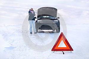 Woman near a broken machine freezes. Around a snowy field. Emergency sign. Winter.