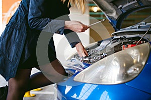 Woman near car`s hood. young blonde in covered parking of shopping center, stands near car with engine compartment bonnet raised,