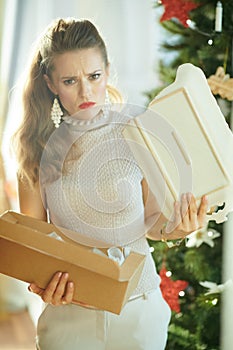 Woman near Christmas tree pulling out broken dish from parcel