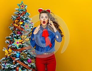 Woman near Christmas tree on yellow background using cell phone