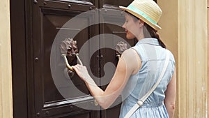 Woman near old wooden door hold handle in form of lion. Female traveler knock on door in slow motion
