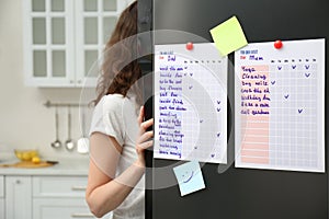 Woman near refrigerator with to do lists on door