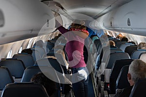 Woman placing suitcase inside overhead compartment in plane